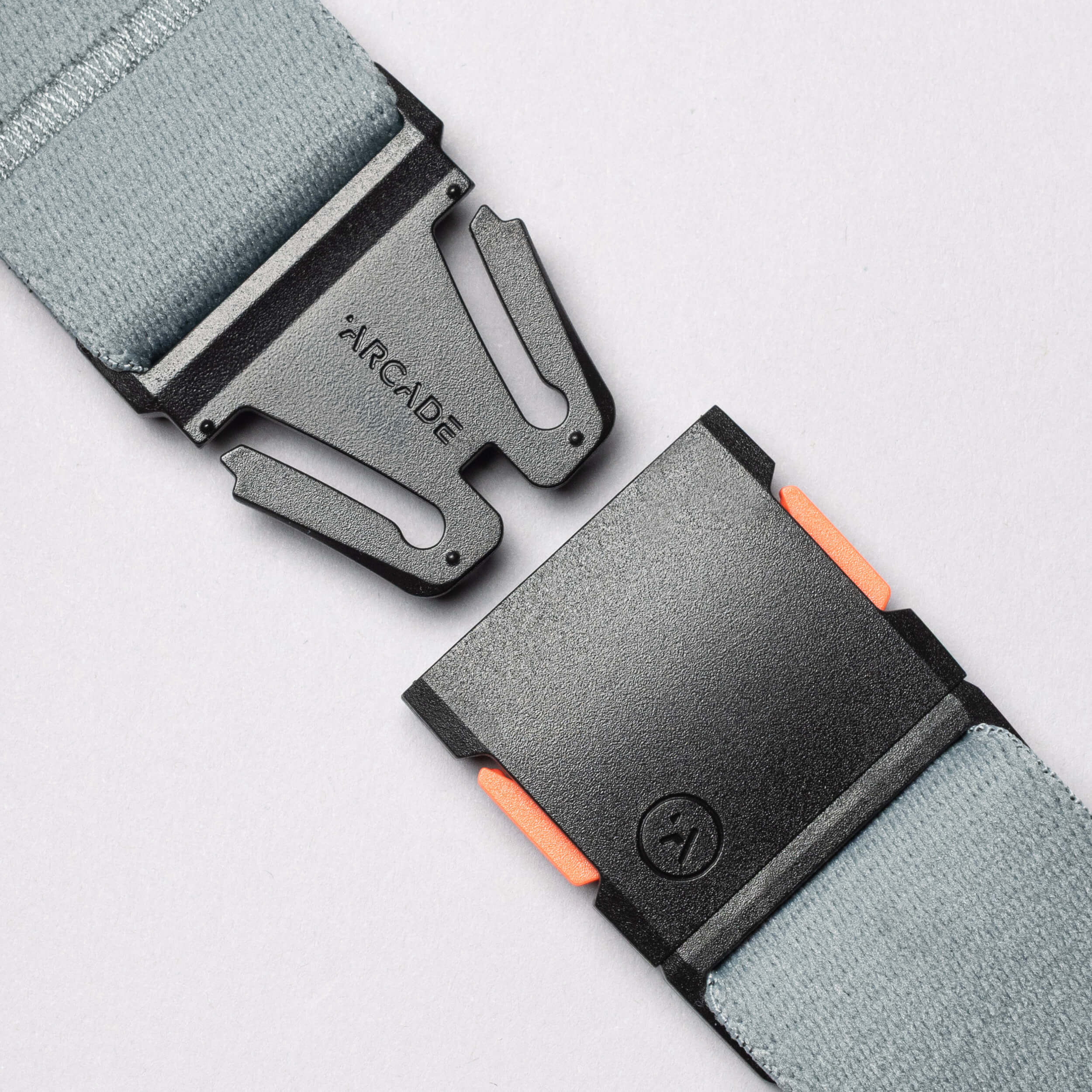 Close-up of a gray elastic Arcade Belt Co. belt by Arcade Belts, featuring a black plastic buckle with orange accents on the clasp, shown separated against a light background.