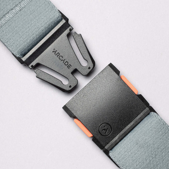 Close-up of a gray elastic Arcade Belt Co. belt by Arcade Belts, featuring a black plastic buckle with orange accents on the clasp, shown separated against a light background.