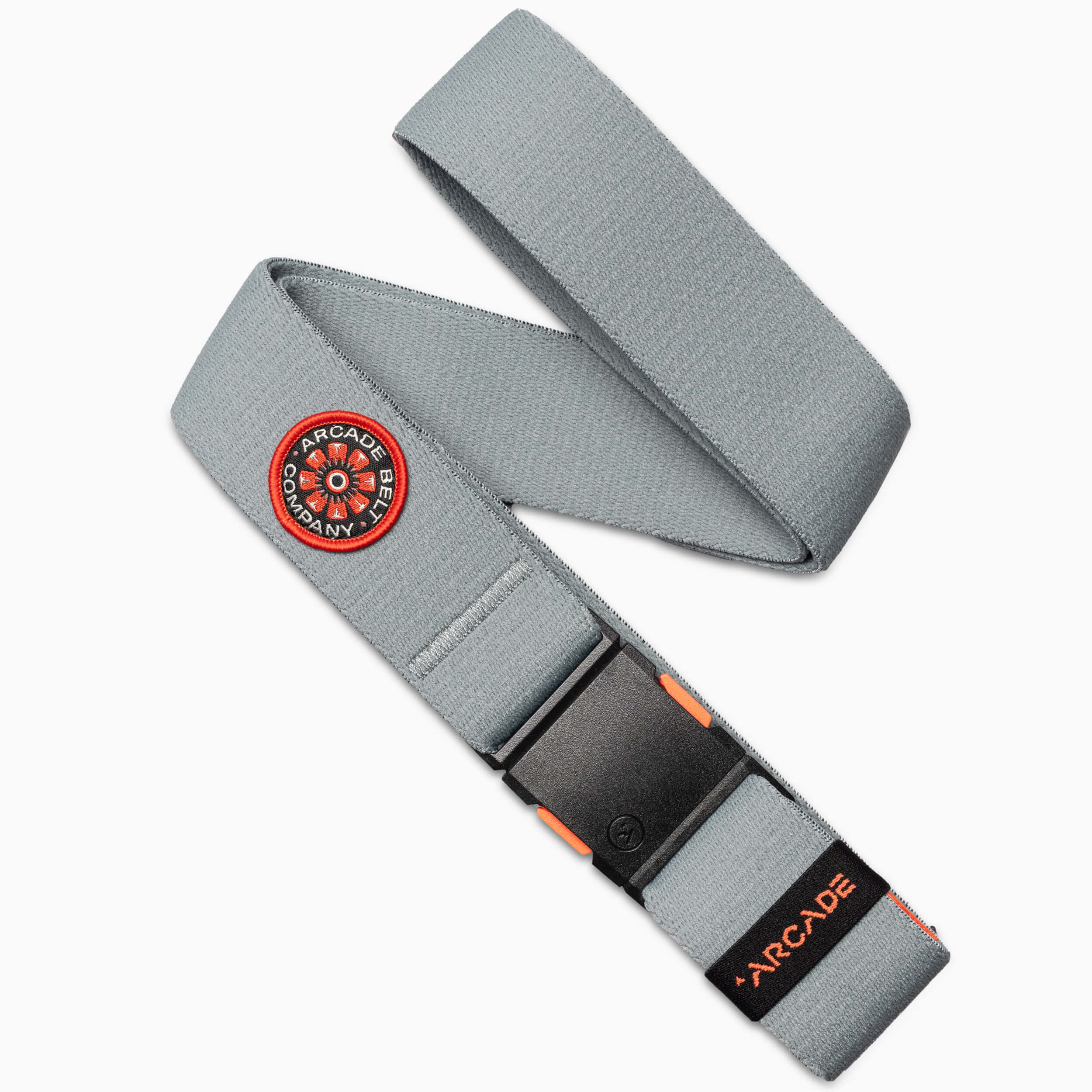 A gray elastic stretch belt from Arcade Belts features a black plastic buckle, an orange ARCADE label, and a circular red, black, and white patch reading Arcade Belt Co.—perfect for travel with flexible stretch webbing.