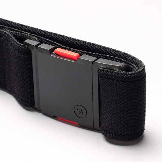 A close-up of the Arcade Belts Recco, a black performance stretch belt with a rectangular black buckle and red accents, displayed on a light gray surface.
