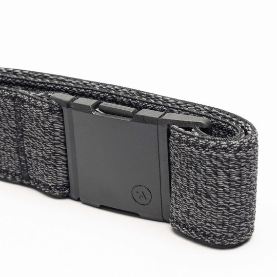 A close-up of the Atlas belt by Arcade Belts, showing its black elastic stretch design with a matte black rectangular buckle and a textured woven pattern with lighter gray threads, neatly folded on a white background.