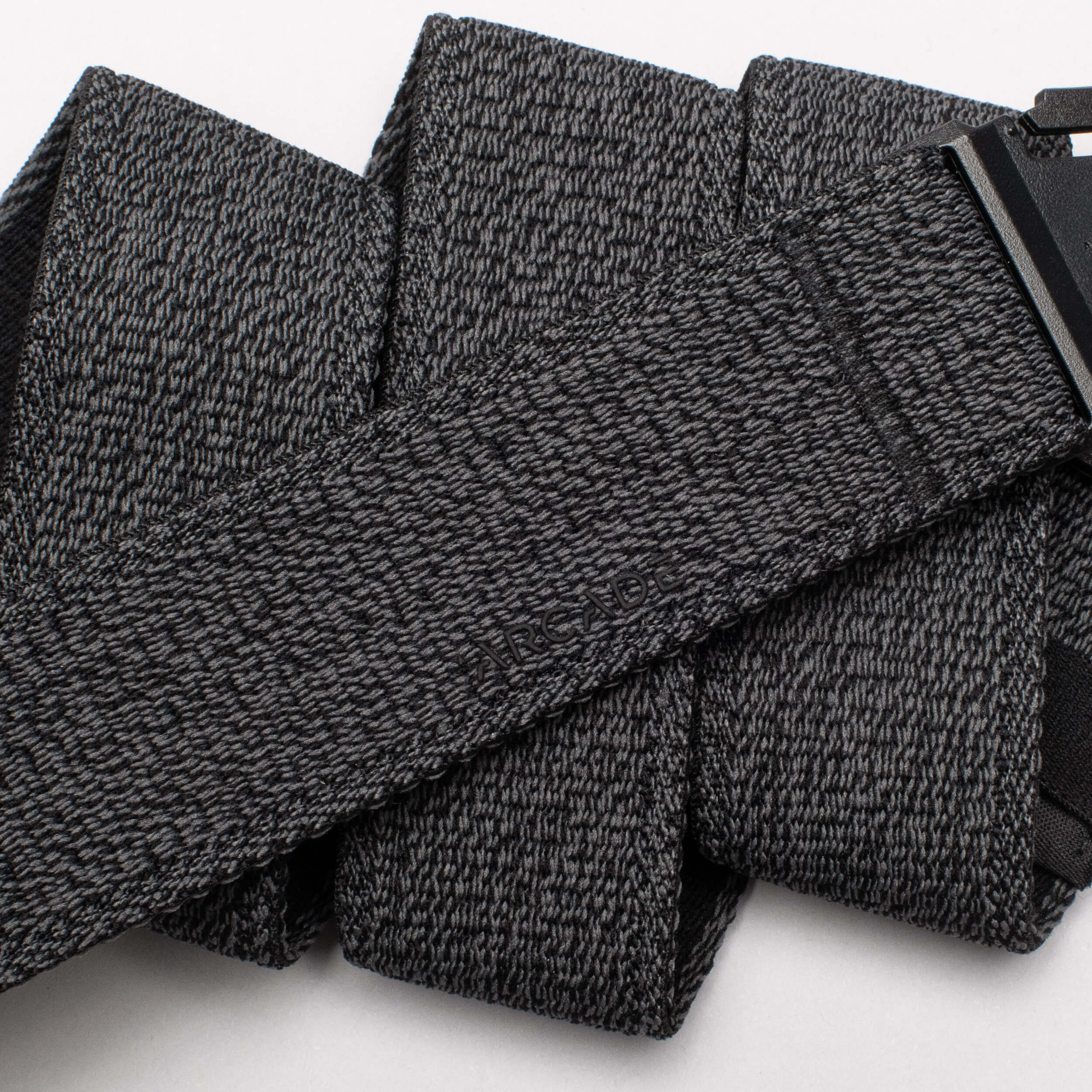 A close-up of the Atlas by Arcade Belts, a black and gray textured travel belt looped in several folds, with its low-profile black buckle partially visible on the right.