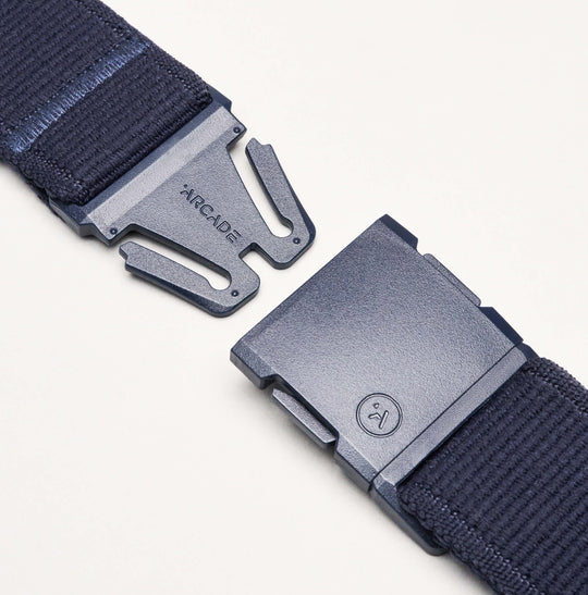 A close-up of the navy blue Atlas Elastic Stretch Belt by Arcade Belts, featuring a metal clasp that’s partially unbuckled, with ARCADE etched on one side and a small circular logo on the other, showcasing its quality craftsmanship.