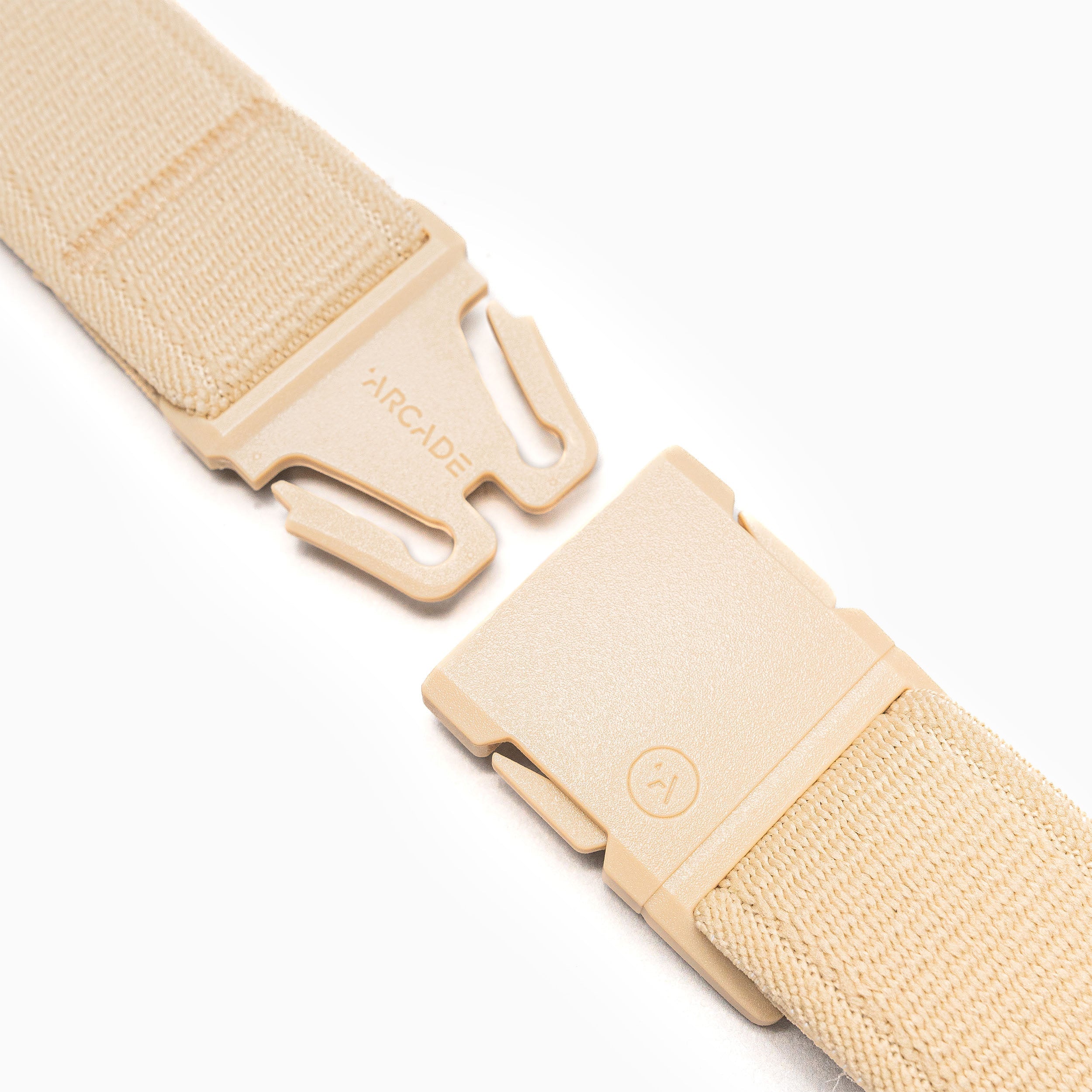 A close-up of the beige Atlas Elastic Stretch Belt by Arcade Belts, showing its plastic buckle slightly open to display the fastening mechanism. ARCADE is engraved on one side. The background is white.
