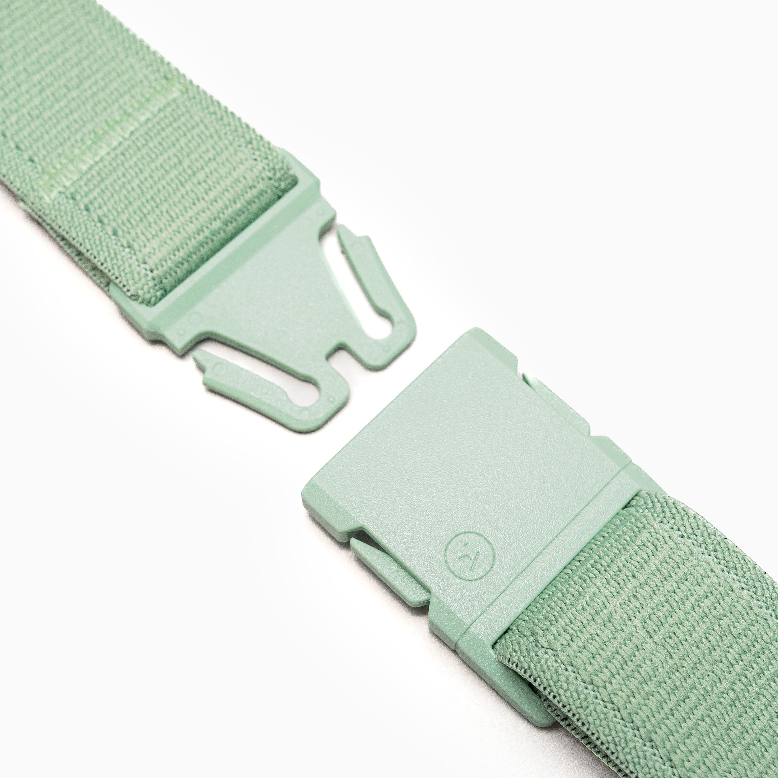 A close-up of the Arcade Belts Atlas shows its green fabric strap with an unfastened plastic buckle, featuring a minimalist smiley face icon, lying on a white background.