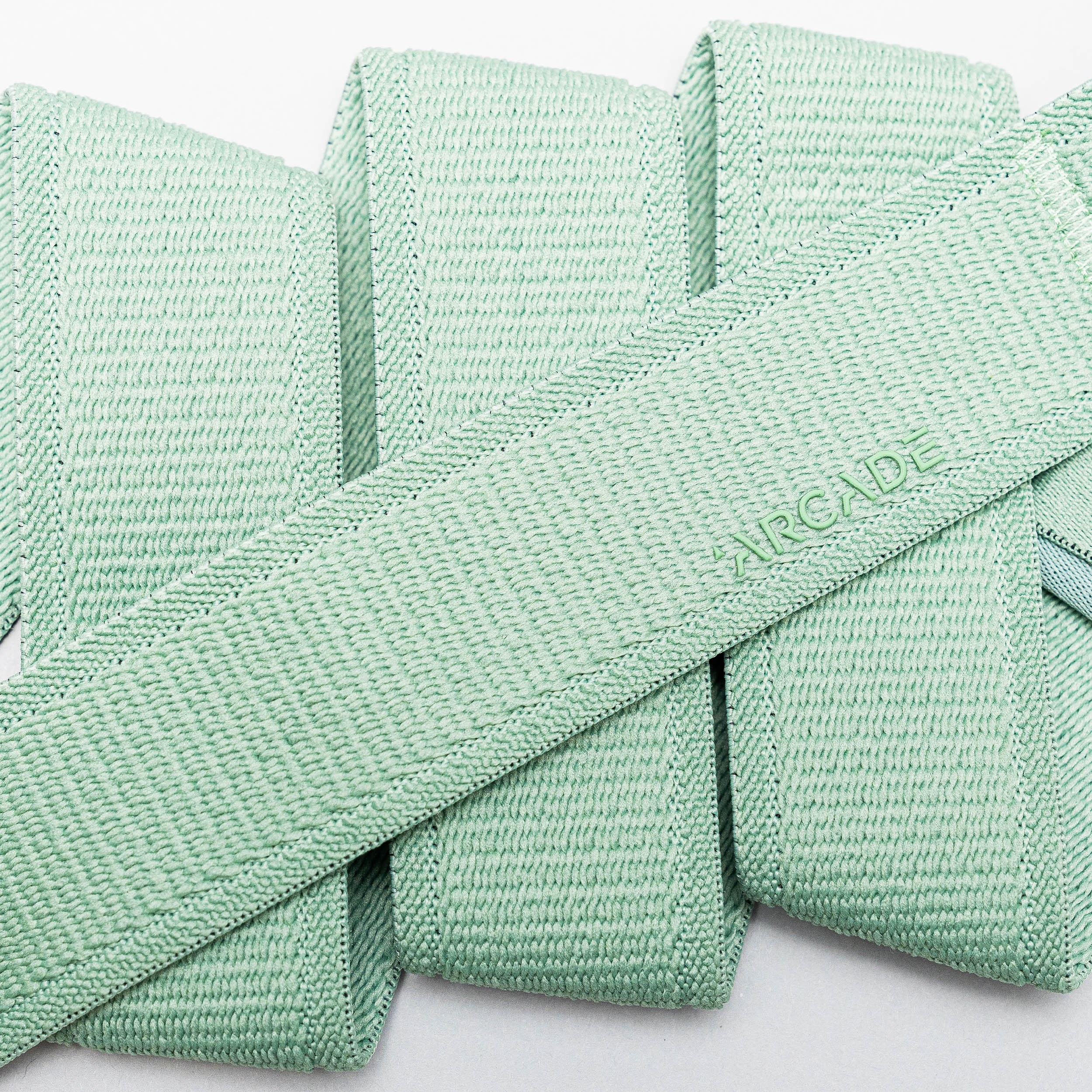 A close-up of several overlapping light mint green Atlas straps by Arcade Belts, crafted from stretch webbing, with ARCADE subtly embossed on one.