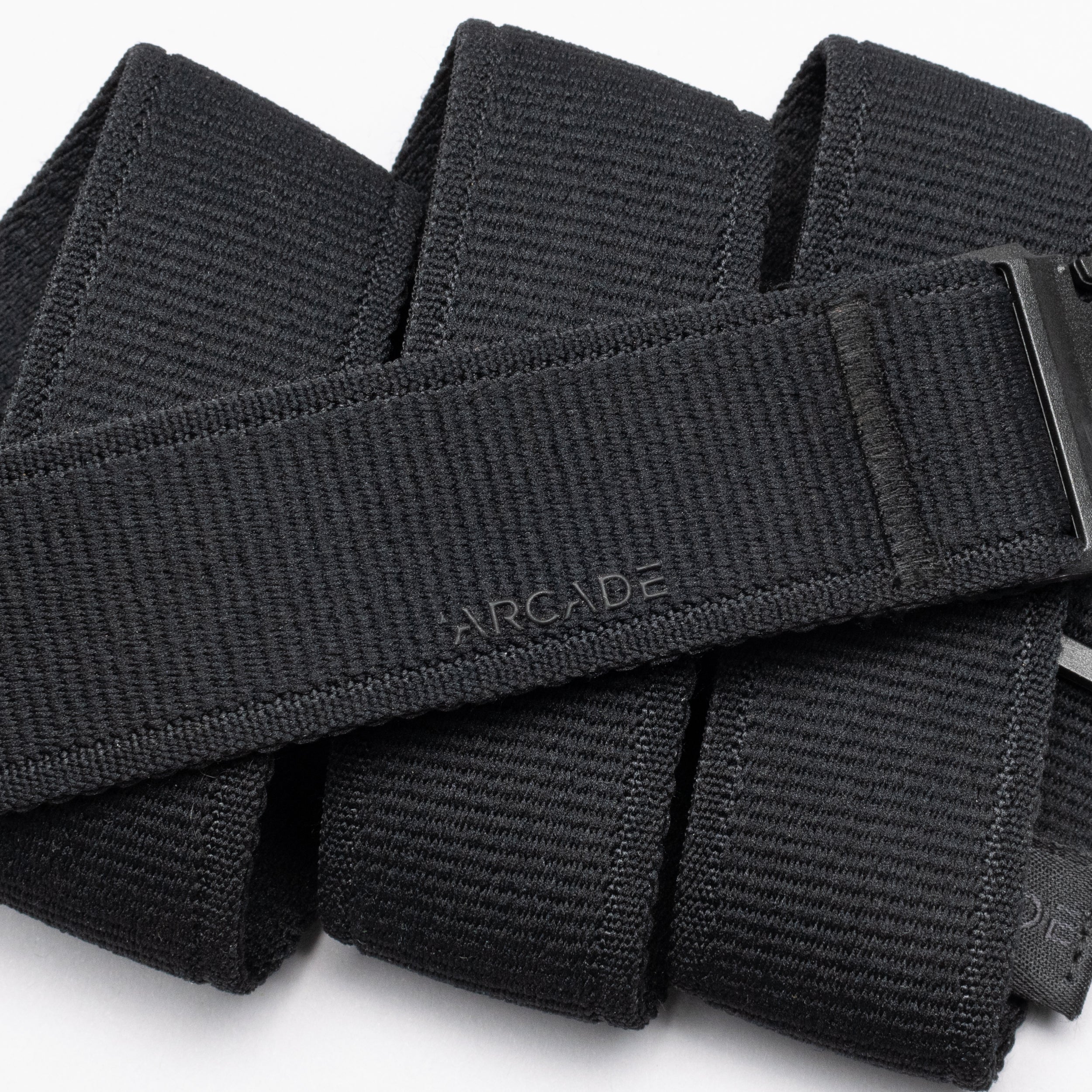 A close-up of the Atlas belt by Arcade Belts, featuring a black low-profile design with a textured surface and a subtle Arcade logo. Coiled with part of its plastic buckle visible—perfect for travel enthusiasts.