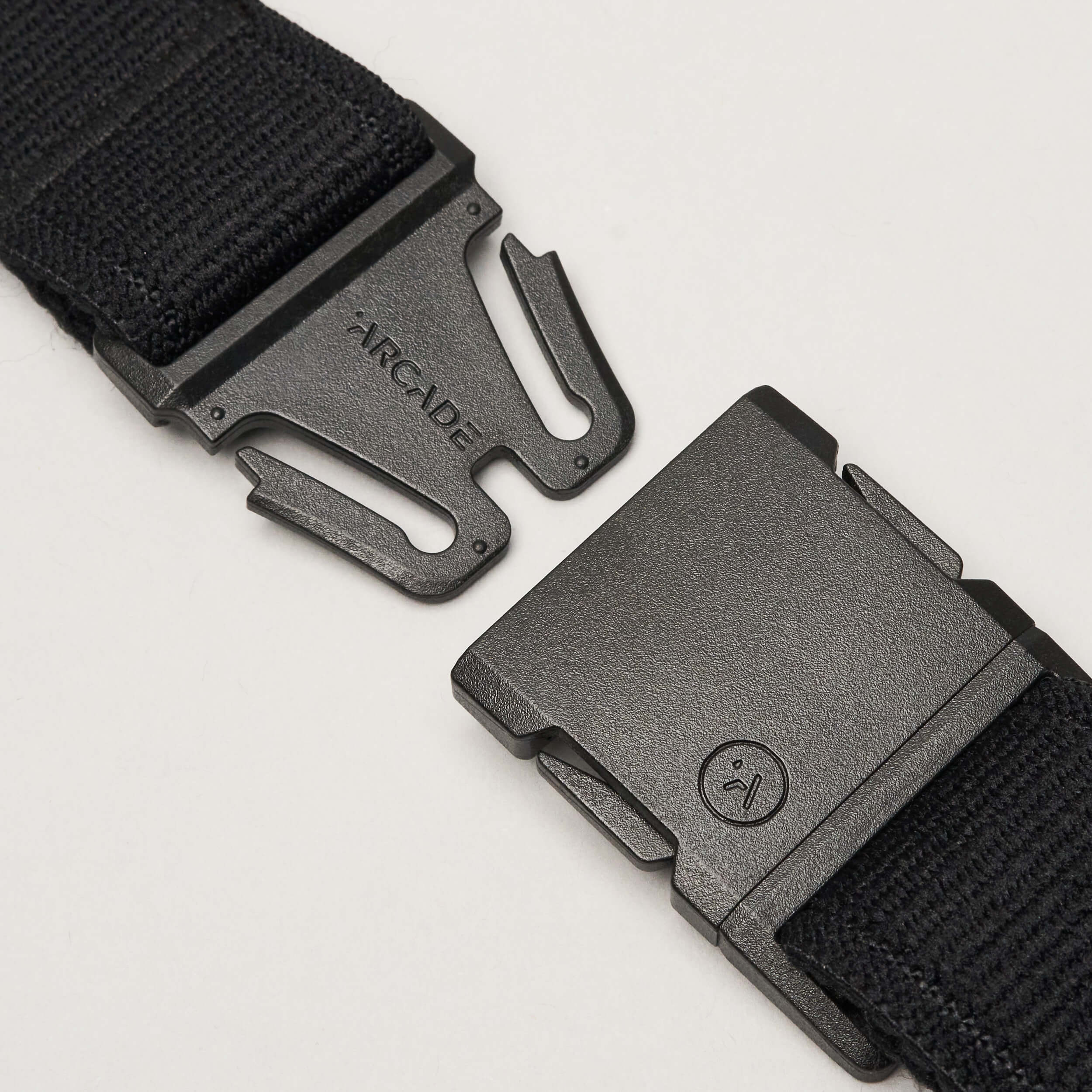 A close-up of the Atlas elastic stretch belt by Arcade Belts in black, featuring a plastic quick-release buckle. The unfastened low-profile buckle shows the Arcade Belts brand name on one side and a small circular face logo on the other.