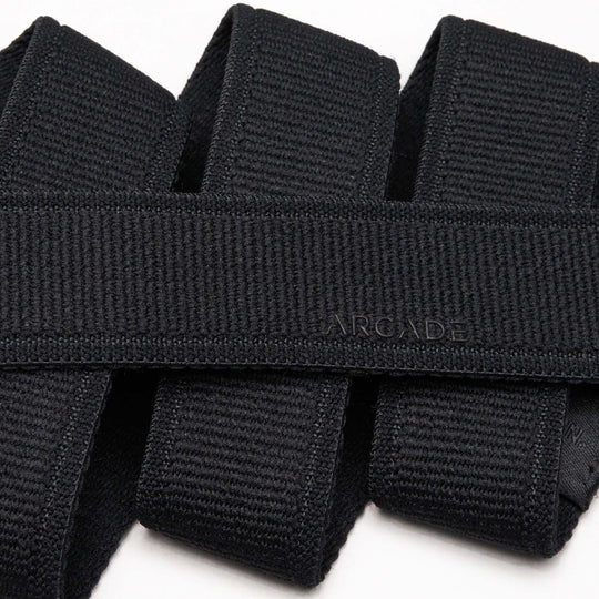 A close-up photo of overlapping black Atlas belts from Arcade Belts, with the word ARCADE subtly embossed on one of the elastic stretch belts near the center.