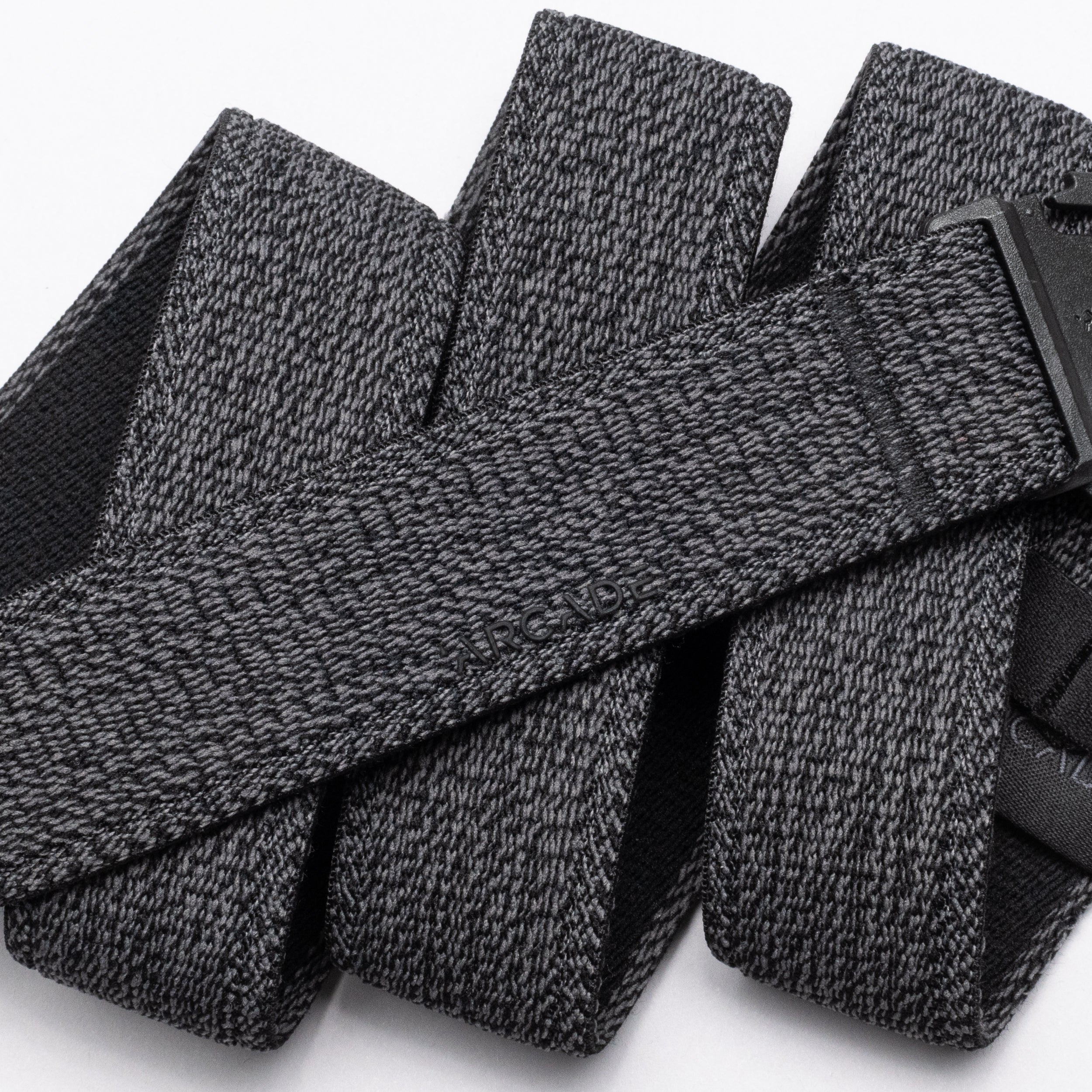 A close-up of the Atlas belt by Arcade Belts showcases its textured gray stretch webbing and black buckle. The elastic belt, looped on a white background, features the ARCADE branding subtly embossed on its surface.
