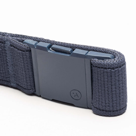 A close-up of the Atlas belt by Arcade Belts in navy blue stretch webbing, featuring a rectangular matte-finish plastic buckle with a small circular logo. The low-profile belt is displayed on a white surface.