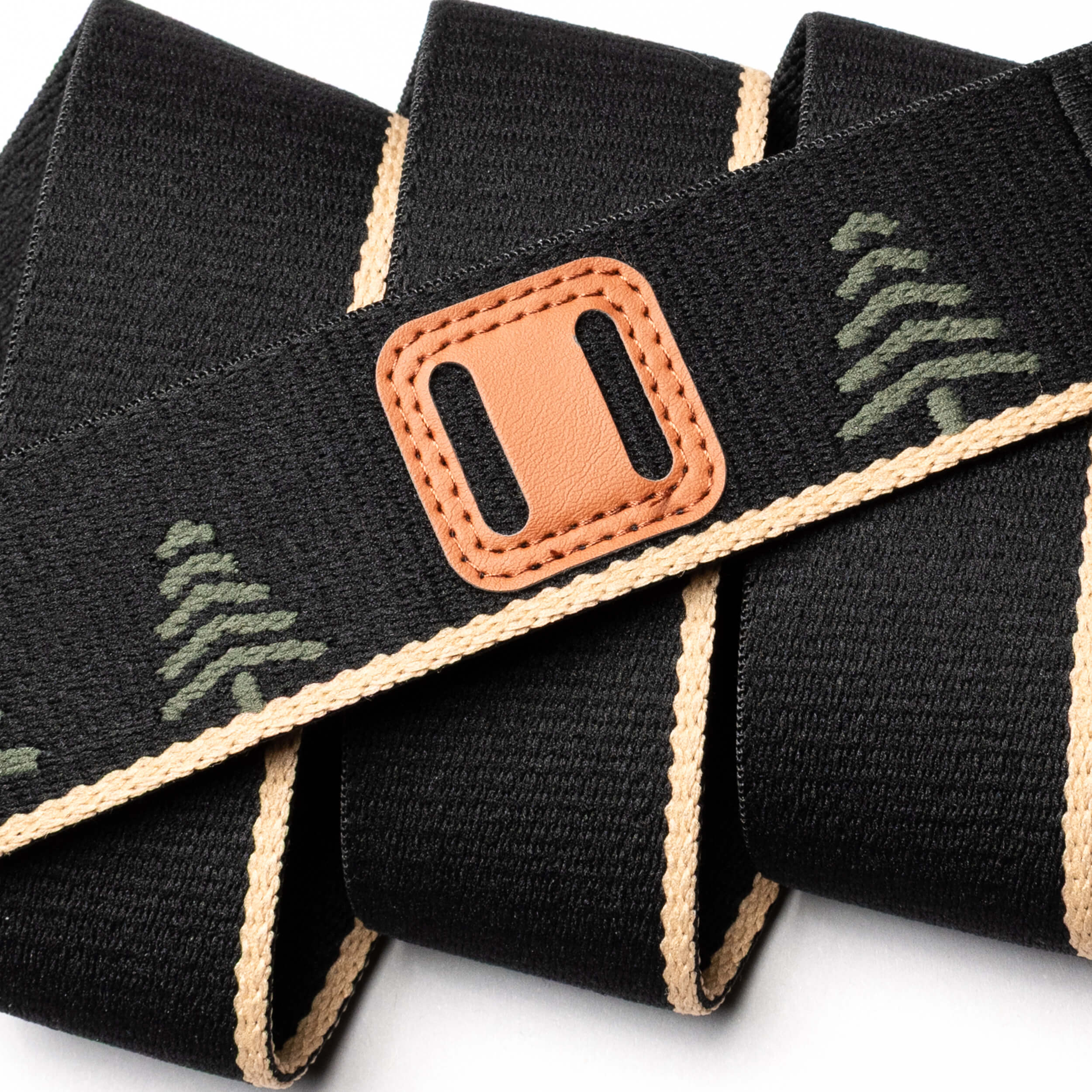 The Arcade Belts Blackwood strap features beige edges, green tree patterns, and a brown leather patch with a rectangular cutout, displayed in overlapping loops on a white background.