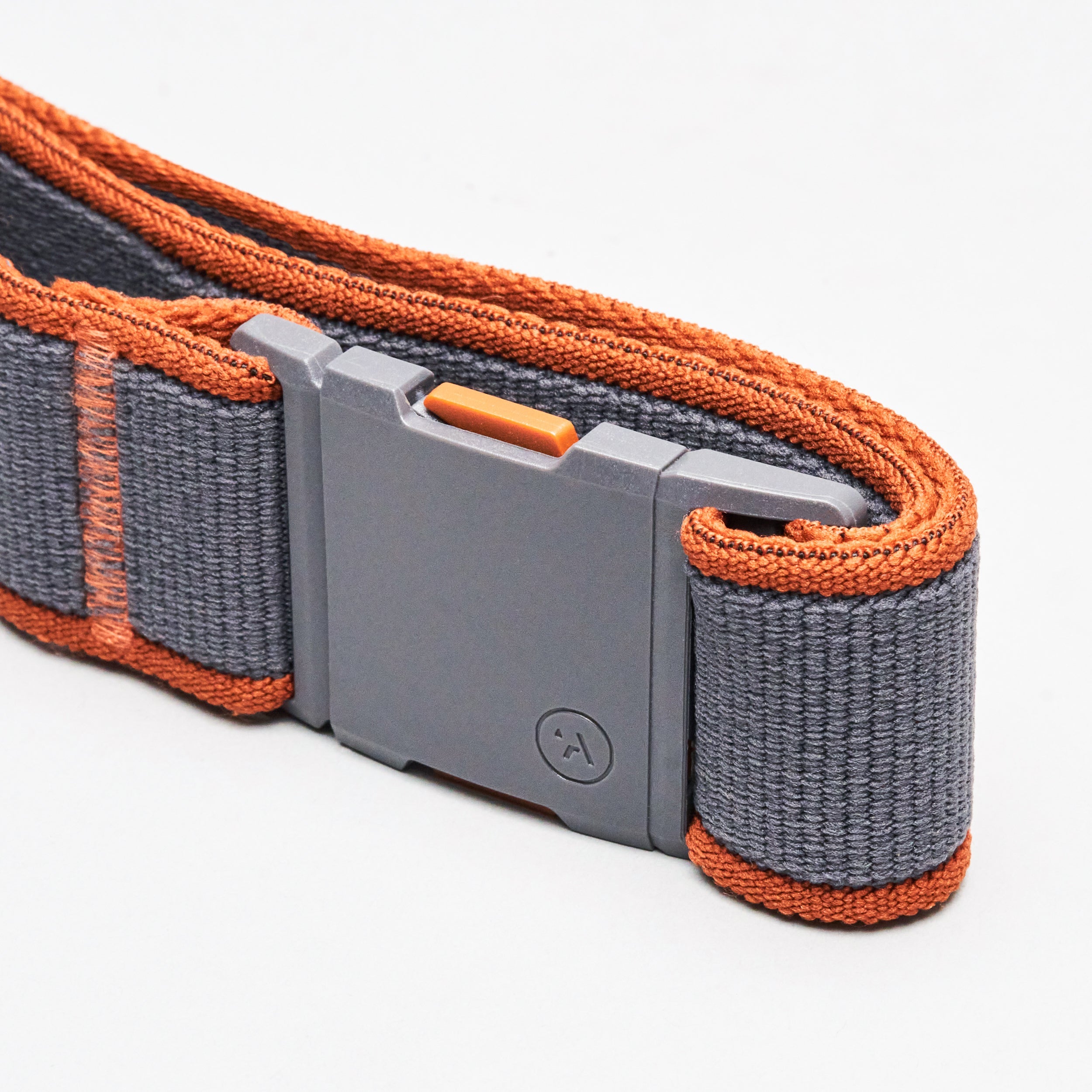 A close-up of the Arcade Belts Carto, a gray belt with orange edges and a plastic rectangular buckle featuring a small logo, set against a white background; its low profile makes it ideal for travel or everyday use.