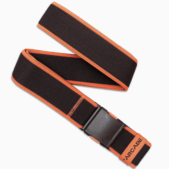 The Arcade Belts Carto is a black elastic stretch belt with orange edges, a black plastic buckle, and ARCADE printed in orange near the tip. Made from stretch webbing, it is shown in a loose zigzag shape.