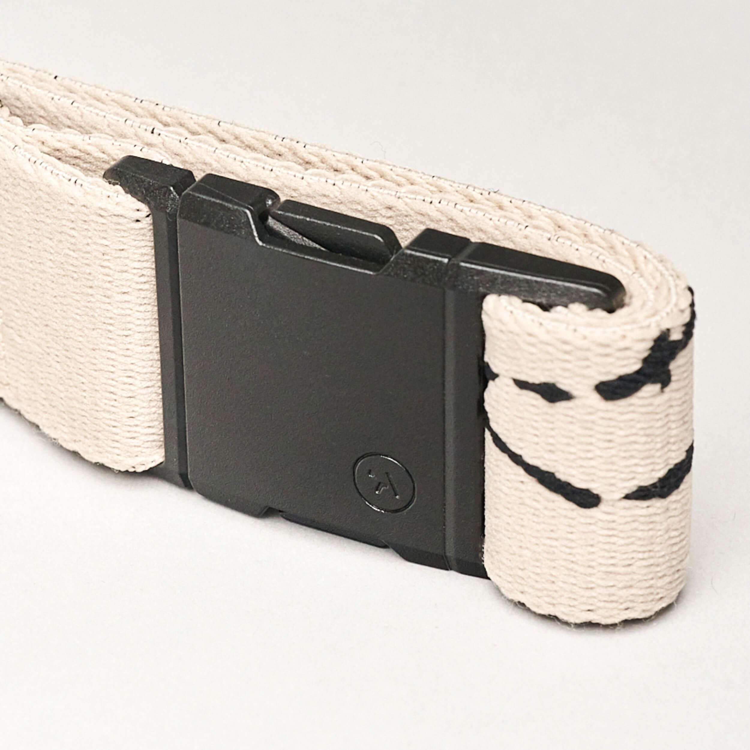 A close-up of a beige fabric strap with black stitching and a rectangular black plastic buckle showcases the sleek design of the Arcade Belts Charmer Slim, set against a light background.