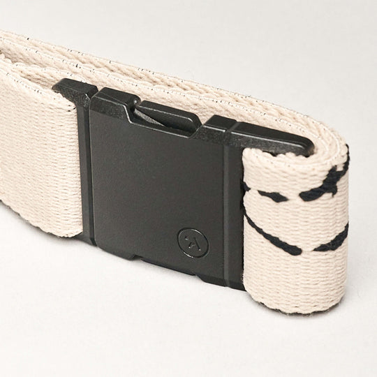 A close-up of a beige fabric strap with black stitching and a rectangular black plastic buckle showcases the sleek design of the Arcade Belts Charmer Slim, set against a light background.