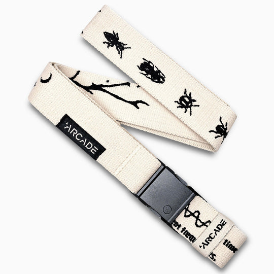 The Arcade Belts Charmer Slim is a beige elastic stretch belt featuring black doodle-style illustrations and a black plastic buckle, shown laid flat on a white background.