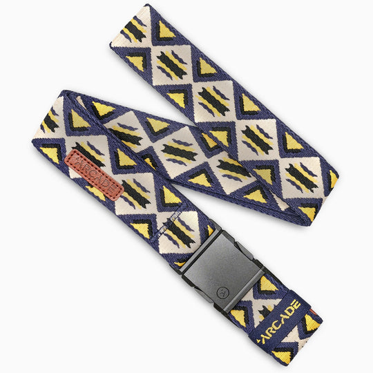 The Arcade Belts Vernan Kee is a fabric belt with blue, yellow, and white triangles and black zigzags inspired by traditional rug patterns. It features a black plastic buckle and a leather patch with the Arcade brand name.