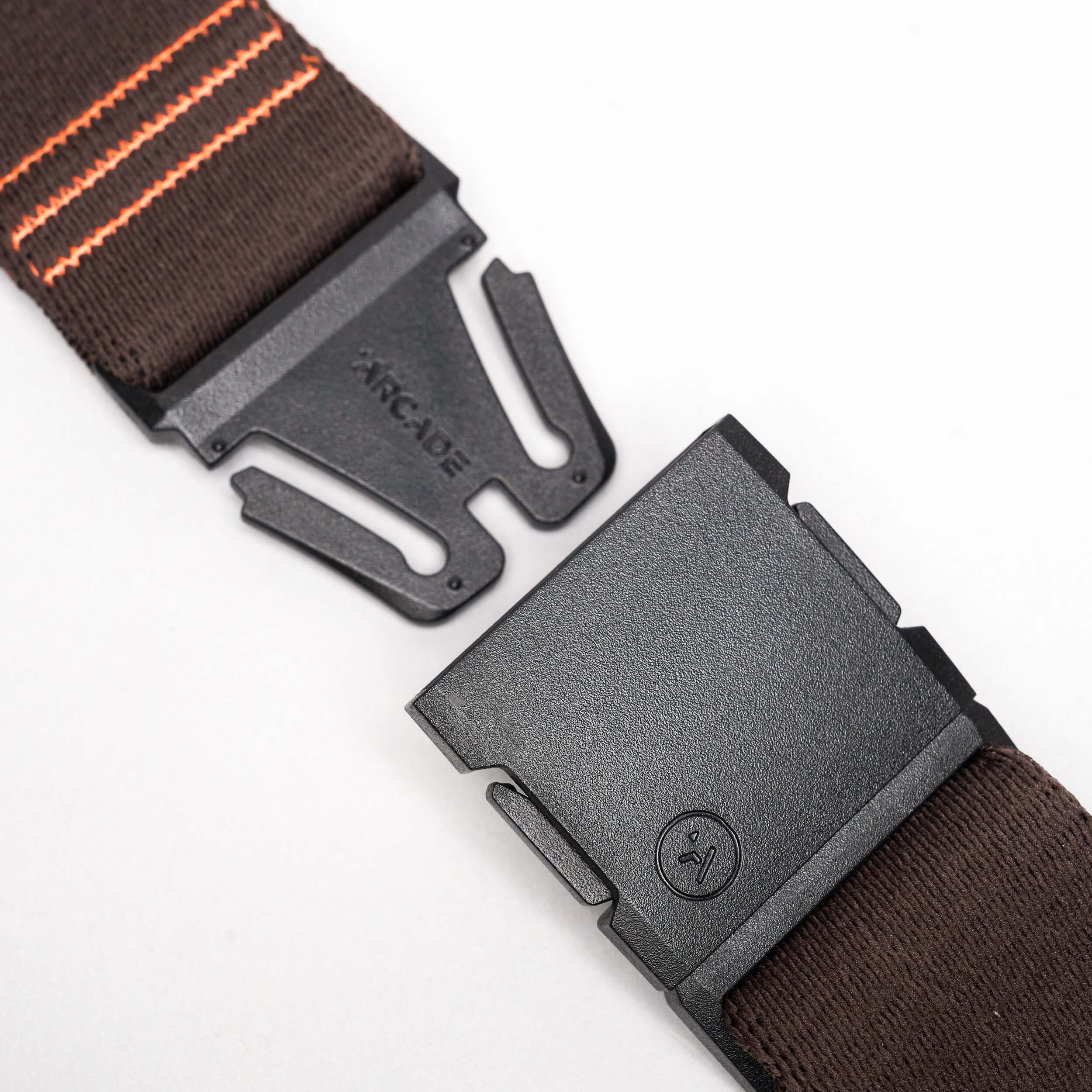 A close-up of the Arcade Belts DDC: a black plastic buckle with logo, attached to a brown stretch webbing strap with orange stripes, shown on a plain white background.