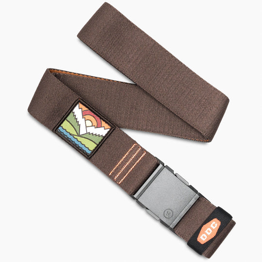 The Arcade Belts DDC is a brown elastic stretch belt with a plastic buckle, orange stitching, a mountain and sunrise embroidered patch, and a small tag with DDC in orange lettering near the end.