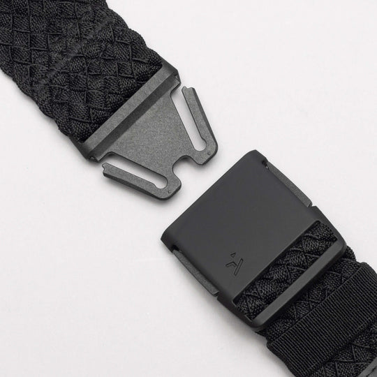 Close-up of the Arcade Belts Futureweave: a black woven belt with a matte black metal buckle, shown partially unclasped against a white background. It features a textured crisscross pattern for a comfortable fit.