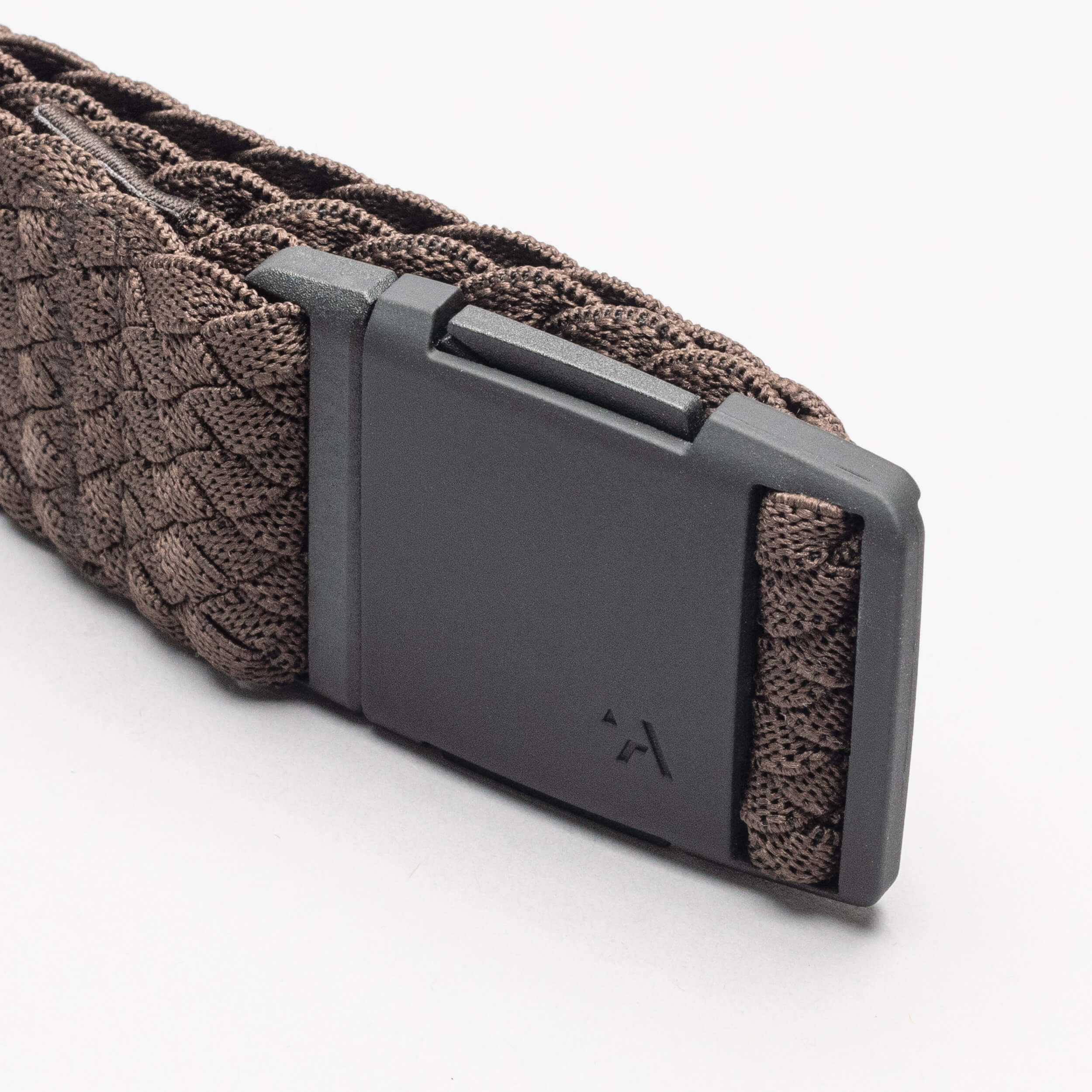 A close-up of the Arcade Belts Futureweave, an elastic stretch belt with a braided brown design and matte black buckle featuring a subtle logo, shown on a white background.