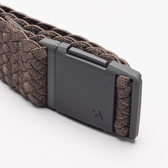 A close-up of the Arcade Belts Futureweave, an elastic stretch belt with a braided brown design and matte black buckle featuring a subtle logo, shown on a white background.