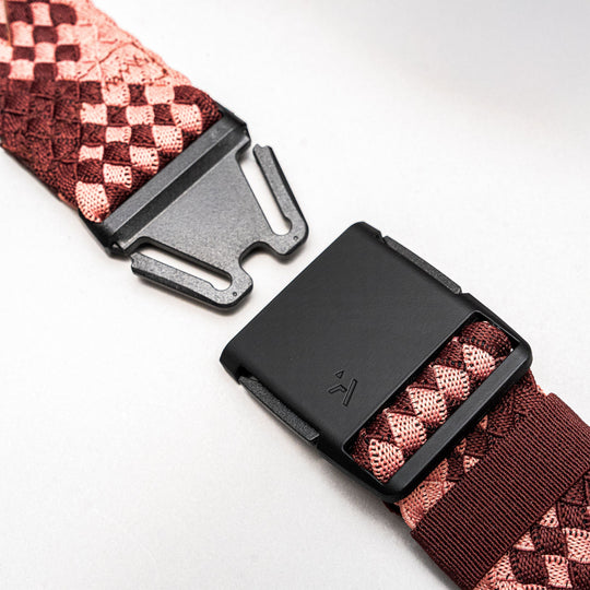 Close-up of the Arcade Belts Futureweave: a black plastic buckle on a red and pink geometric woven strap, shown unclasped on a light background—perfect for travelers seeking a low-profile belt.