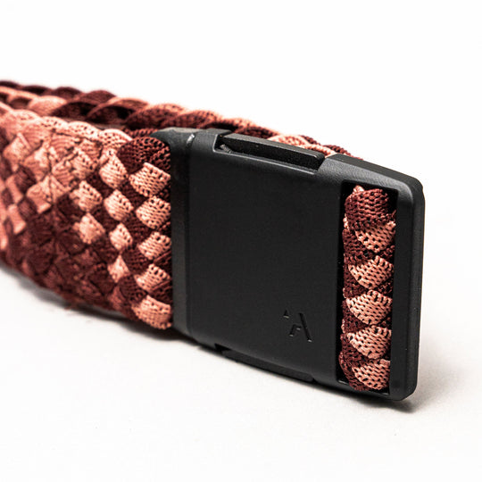 A close-up of the Arcade Belts Futureweave Elastic Stretch Belt with a pink and burgundy pattern and a matte black rectangular buckle featuring a small triangular logo, shown against a plain white background.