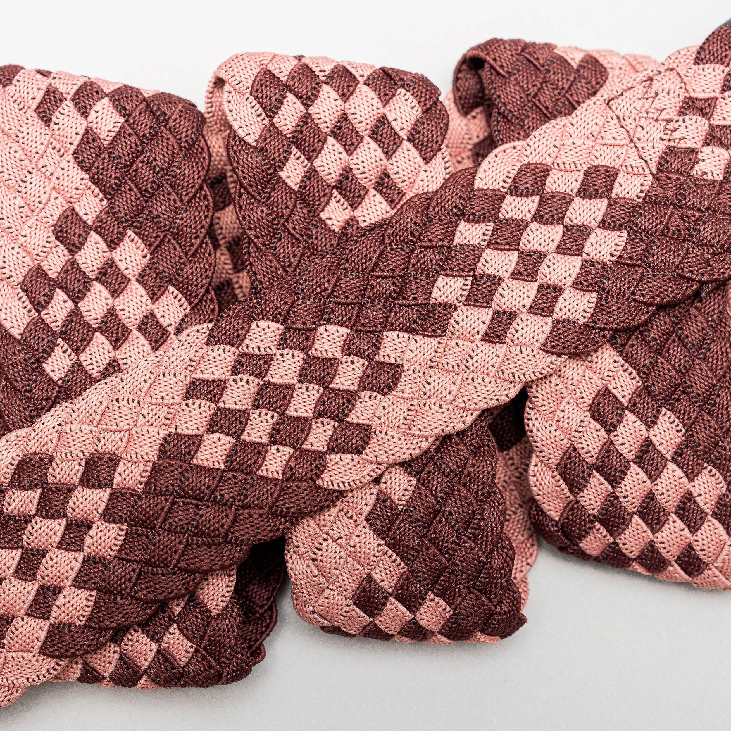 Close-up of Arcade Belts Futureweave, featuring intricately woven ribbons in light pink and dark maroon, creating a geometric checkered pattern with a textured look reminiscent of stretch webbing in an elastic belt.