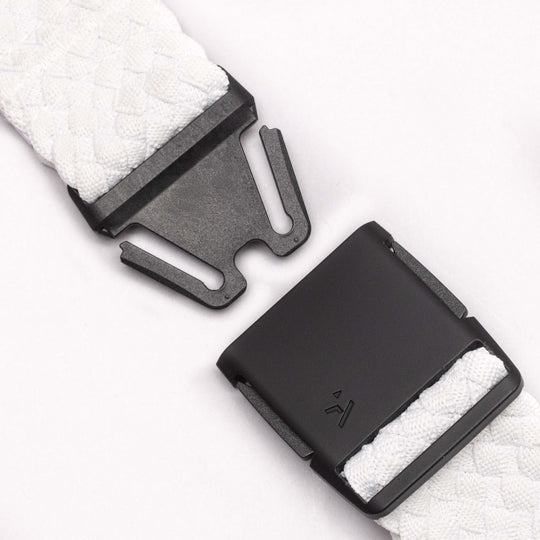 A close-up of the Arcade Belts Futureweave shows a black metal buckle with interlocking prongs and woven white stretch webbing, plus an engraved symbol—ideal for travel.