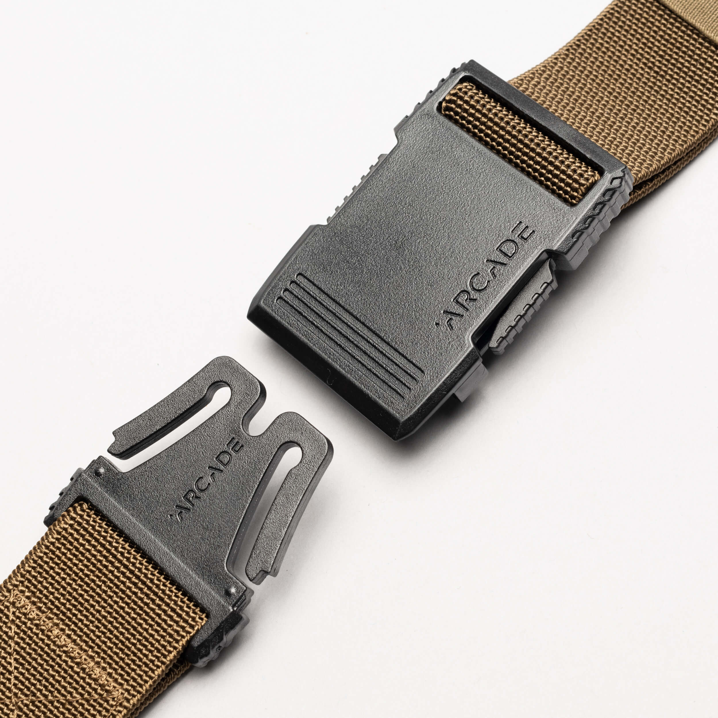 A close-up of the Arcade Belts Hardware, a brown elastic stretch belt with a black plastic buckle—partially unclasped and set against a white background. The ARCADE logo is visible on both parts of the low-profile buckle.