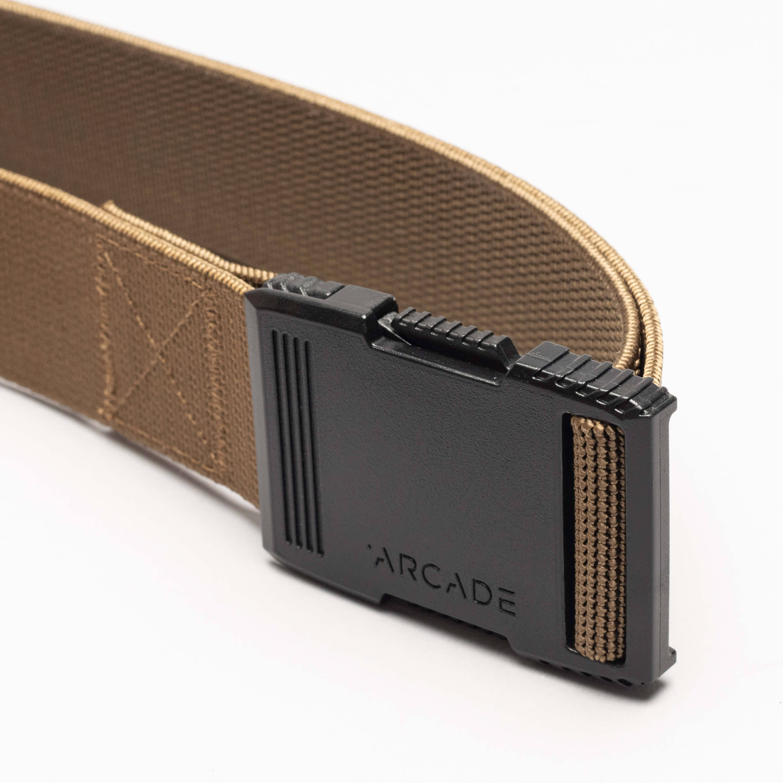 A close-up of the Arcade Belts Hardware, a tan elastic stretch belt with a low-profile black plastic buckle engraved with ARCADE, laid out on a plain white background.