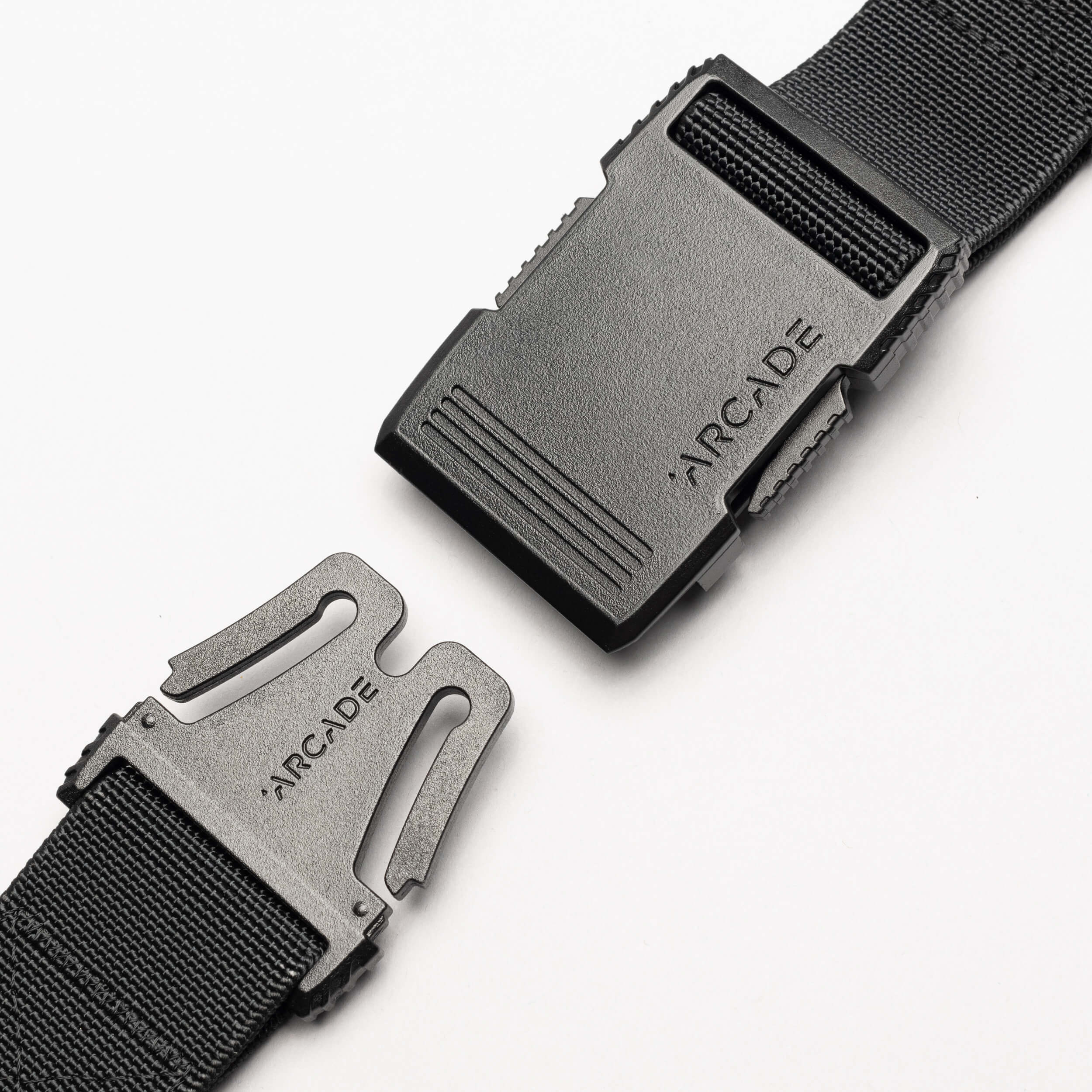 Close-up of the Arcade Belts Hardware black stretch belt with a plastic buckle, partially unclasped. Both buckle pieces are engraved with ARCADE. The sleek, low profile design is highlighted against a plain white background.
