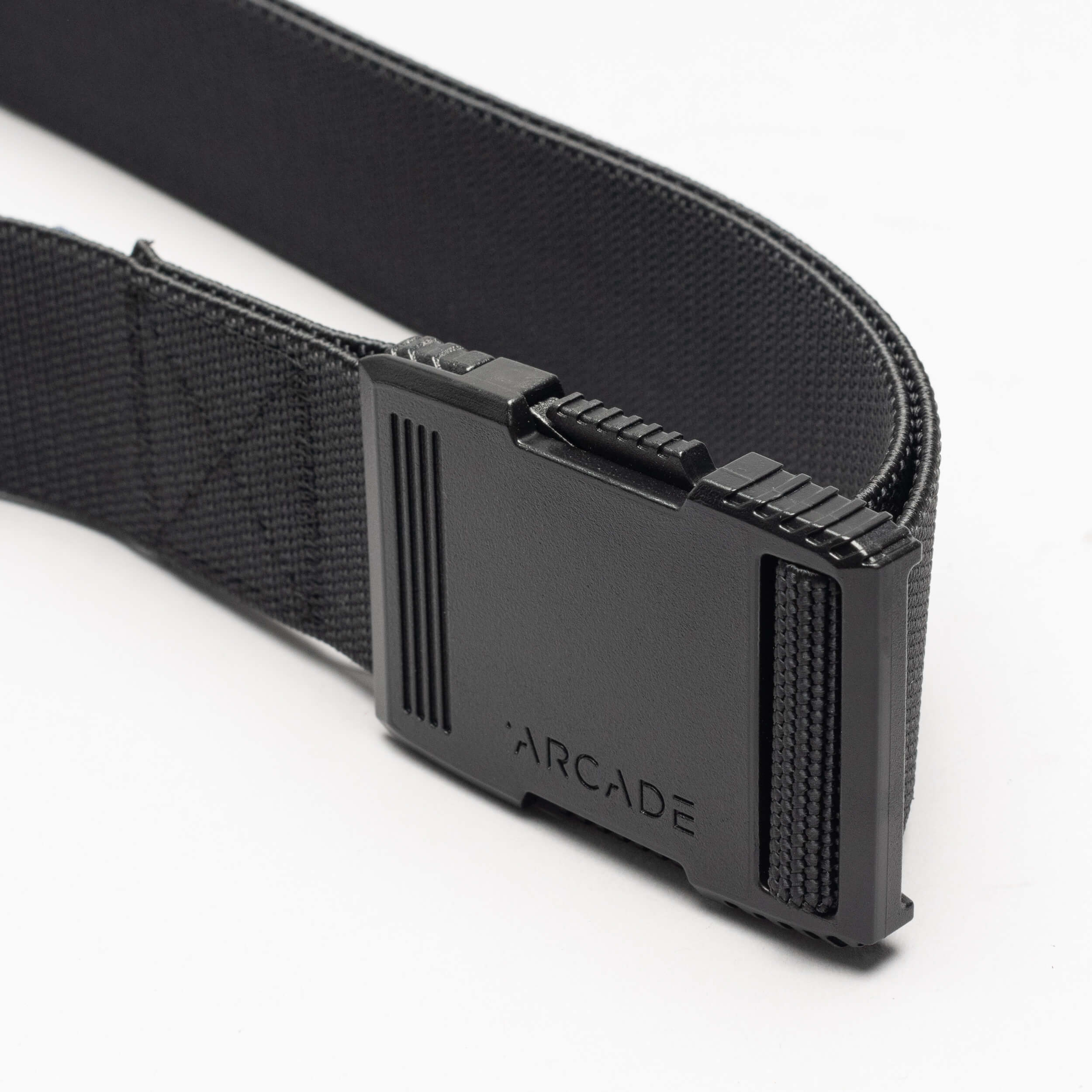 A close-up of the Arcade Belts Hardware: a black elastic stretch belt with a rectangular black plastic buckle engraved with “ARCADE,” shown against a white background.