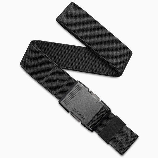 The Arcade Belts Hardware is a black adjustable travel belt with stretch webbing and a textured rectangular black plastic buckle featuring the word ARCADE embossed on it, shown partially unrolled on a white background.