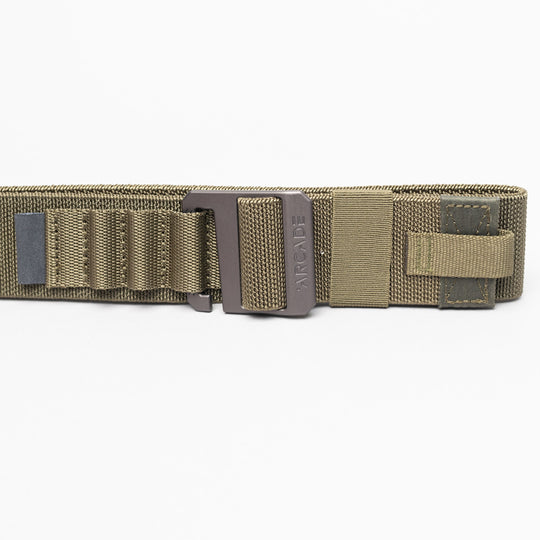 A close-up of the olive green Arcade Belts Hardware Alu tactical belt with a metal buckle, reinforced stitching, webbing loops, and Velcro strap. This low-profile belt offers durability and comfort against a white background.