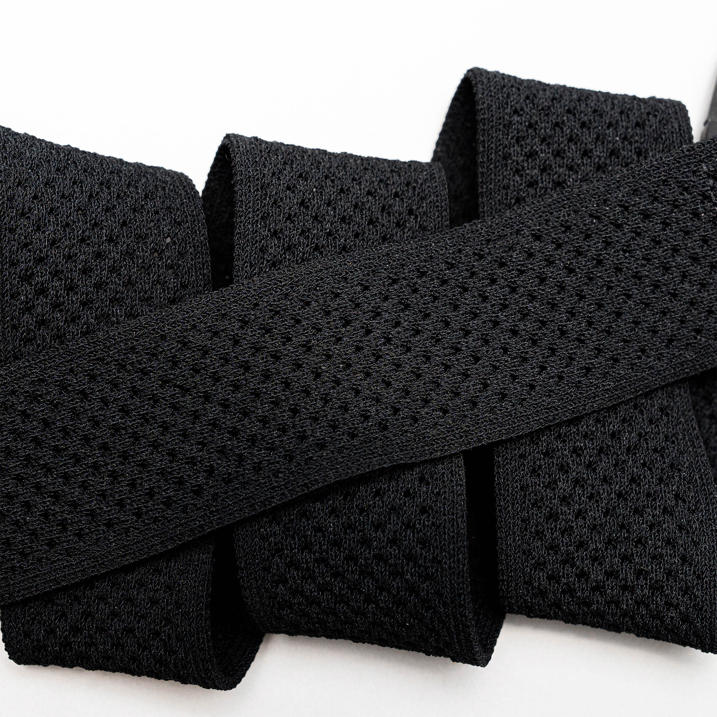 Close-up of the black Momentum elastic stretch belt by Arcade Belts, featuring a mesh-like texture and folded in a zigzag shape against a white background.