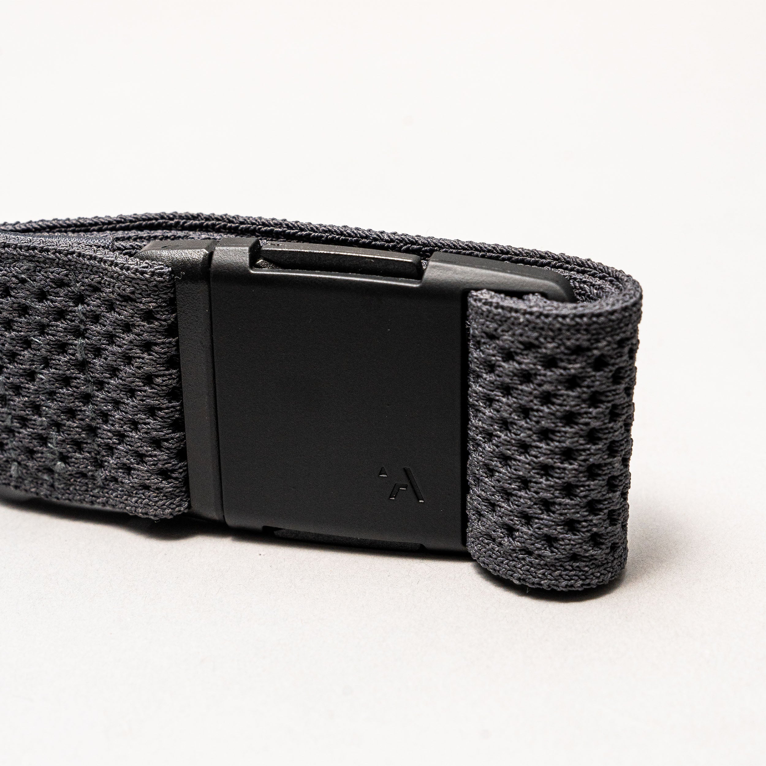 A close-up of the Arcade Belts Momentum strap shows its black textured fabric and rectangular black plastic buckle on a light grey background, highlighting its signature low-profile design.