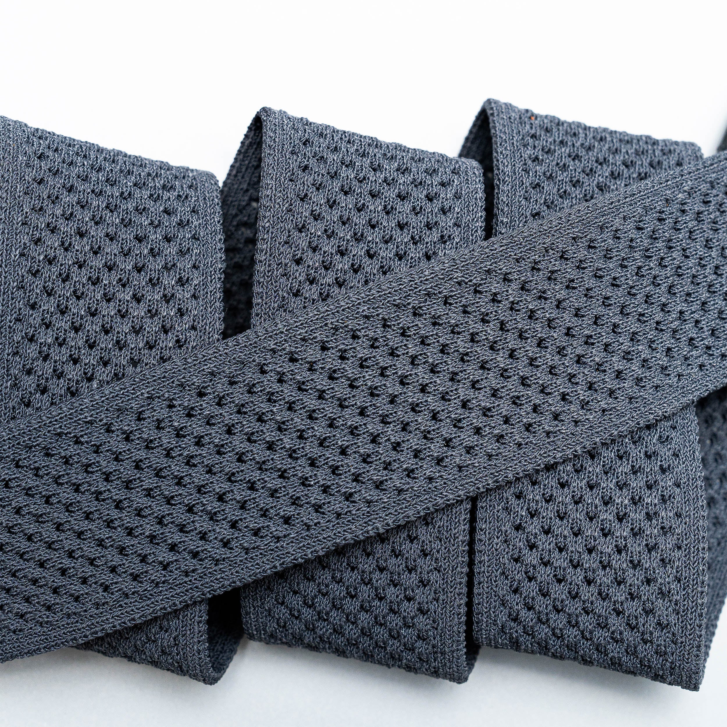 A close-up of the textured, dark gray Momentum elastic band by Arcade Belts, featuring a perforated mesh-like pattern and shown in overlapping folds on a white background.