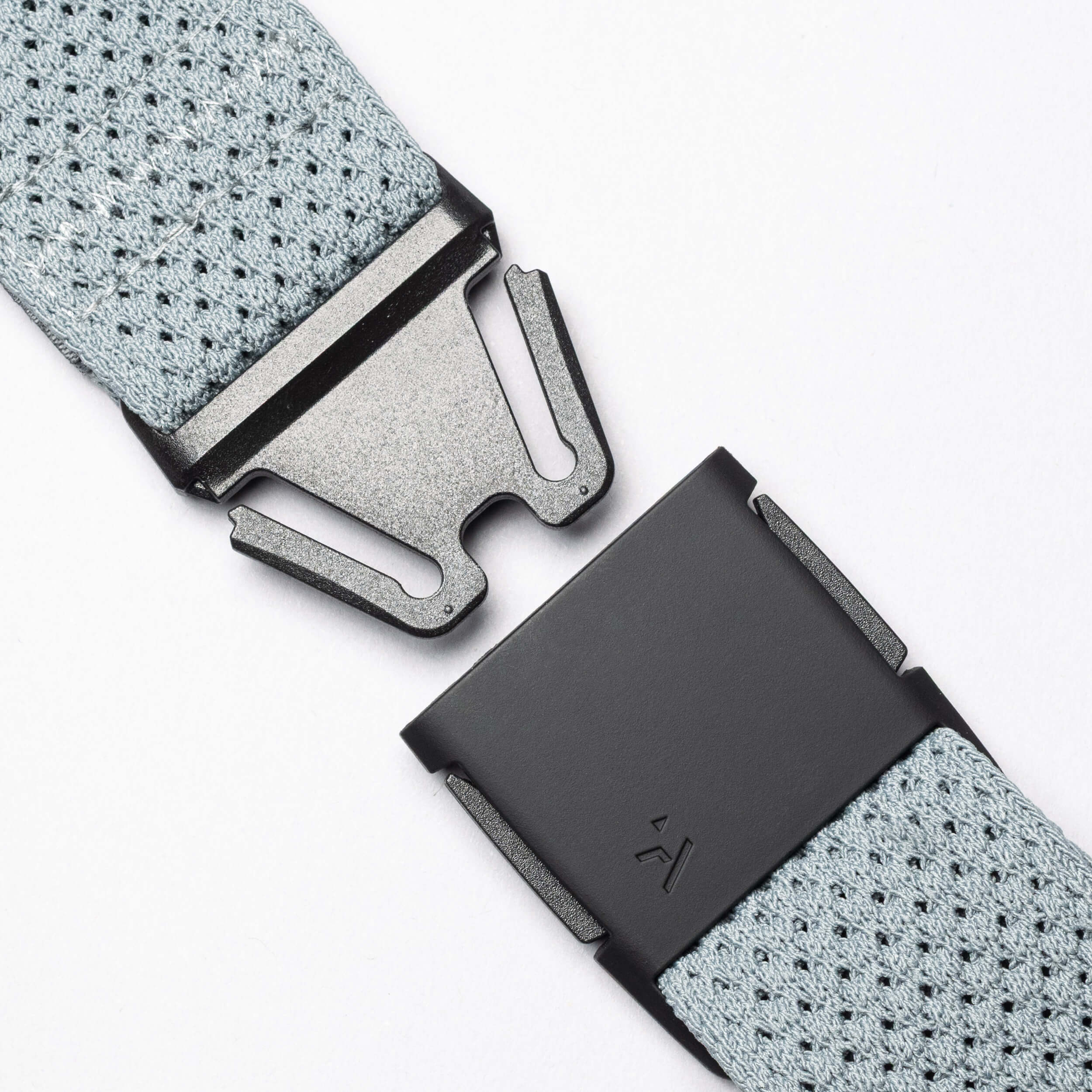 Close-up of the Arcade Belts Momentum: a grey stretch webbing belt with a black metal quick-release buckle shown apart on a white background, illustrating its modern style and secure fastening.