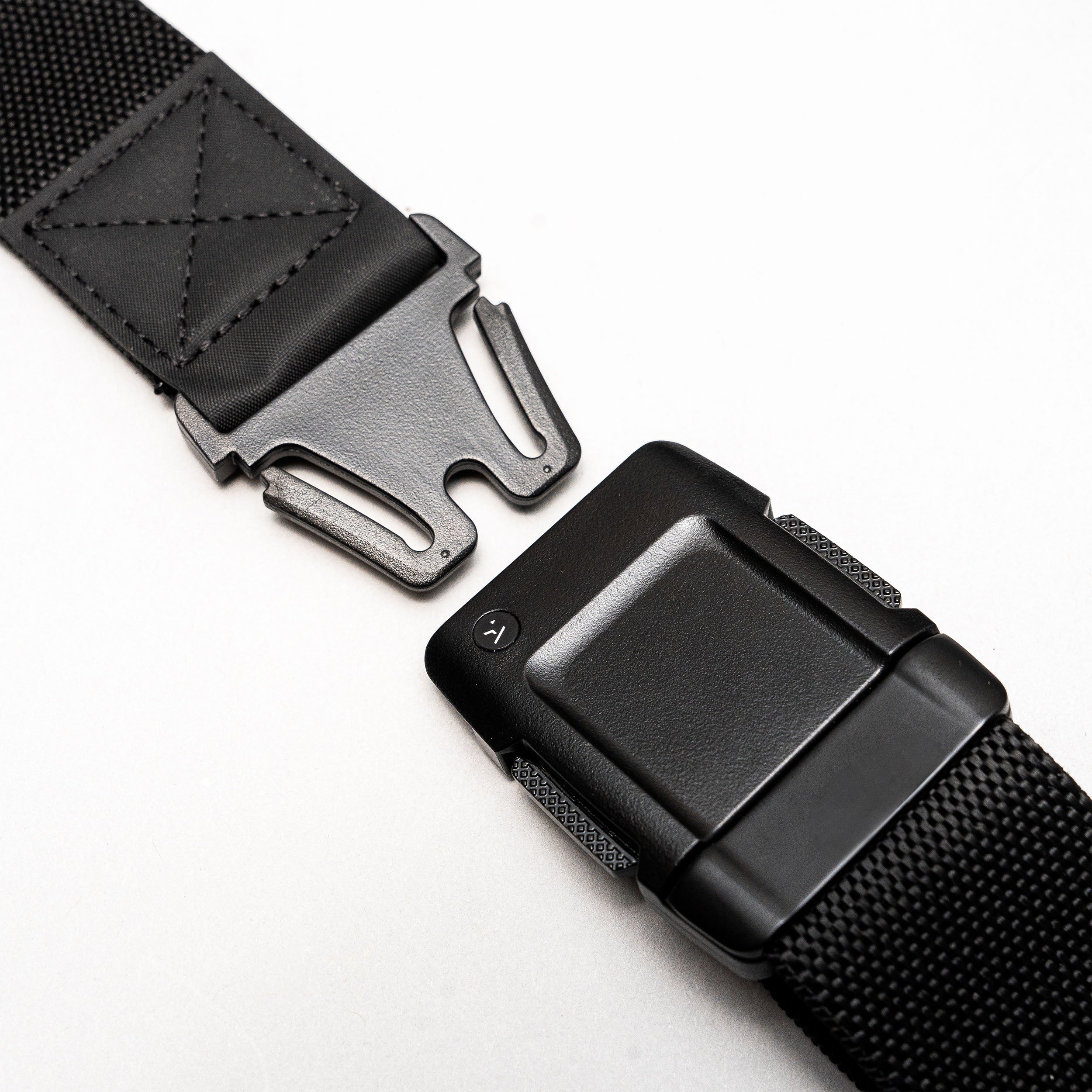 Close-up of the Arcade Belts Motion: a black low profile belt with a metal quick-release buckle, shown partially unfastened on a light background. Made from sturdy, textured stretch webbing for lasting durability and flexible comfort.