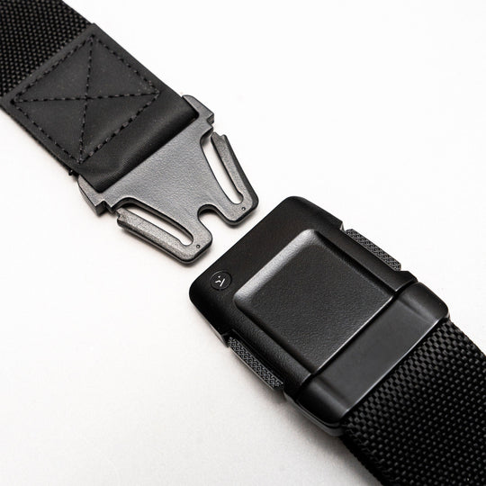Close-up of the Arcade Belts Motion: a black low profile belt with a metal quick-release buckle, shown partially unfastened on a light background. Made from sturdy, textured stretch webbing for lasting durability and flexible comfort.