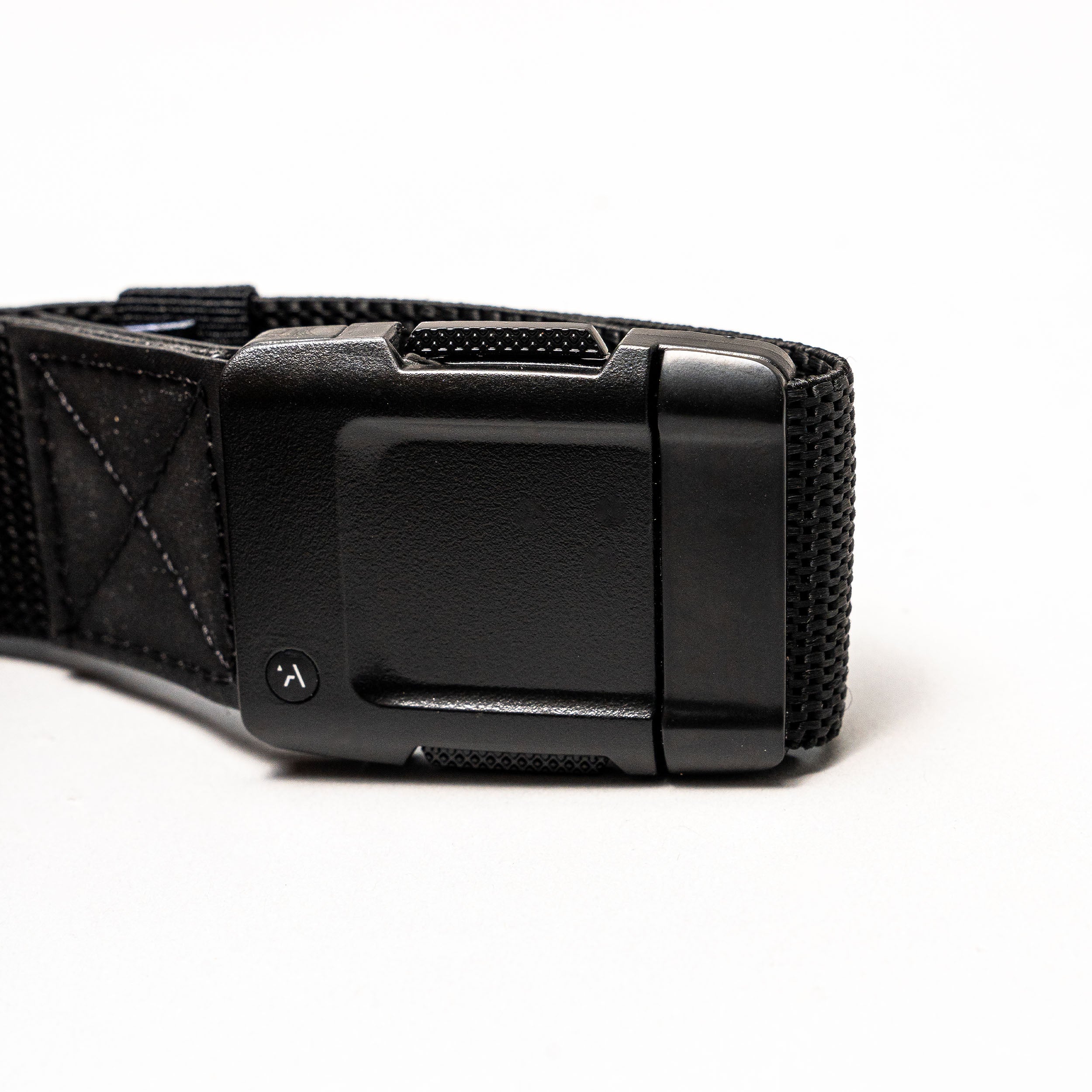 Close-up of the Arcade Belts Motion: a black fabric strap with a rectangular, textured plastic buckle on a white background. The buckle has a small round button with a curved arrow for secure fastening and easy adjustment—perfect for travel.