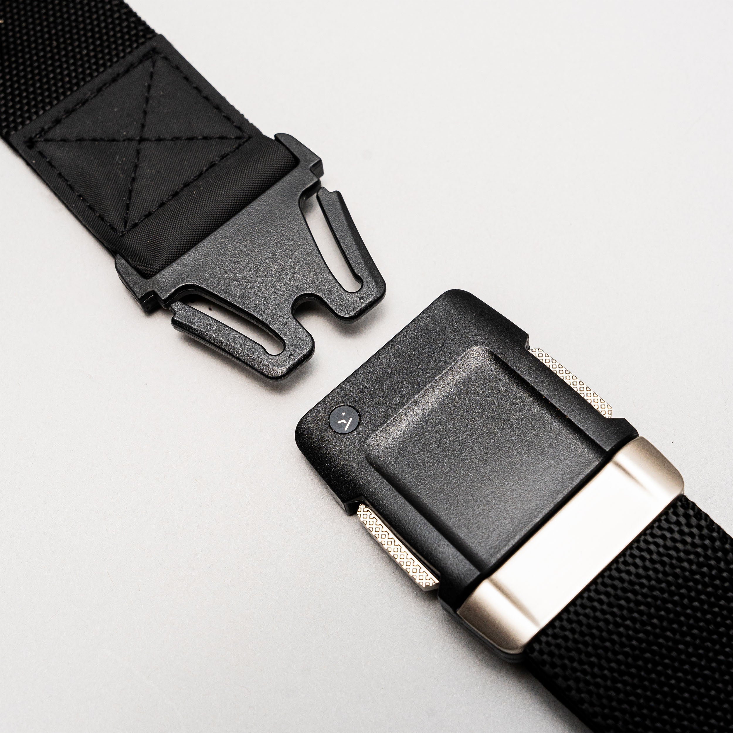 Close-up of the Arcade Belts Motion: a black nylon belt with a sturdy, quick-release black plastic buckle featuring metallic accents. The partially unfastened buckle highlights its clean, modern design against a light gray background.
