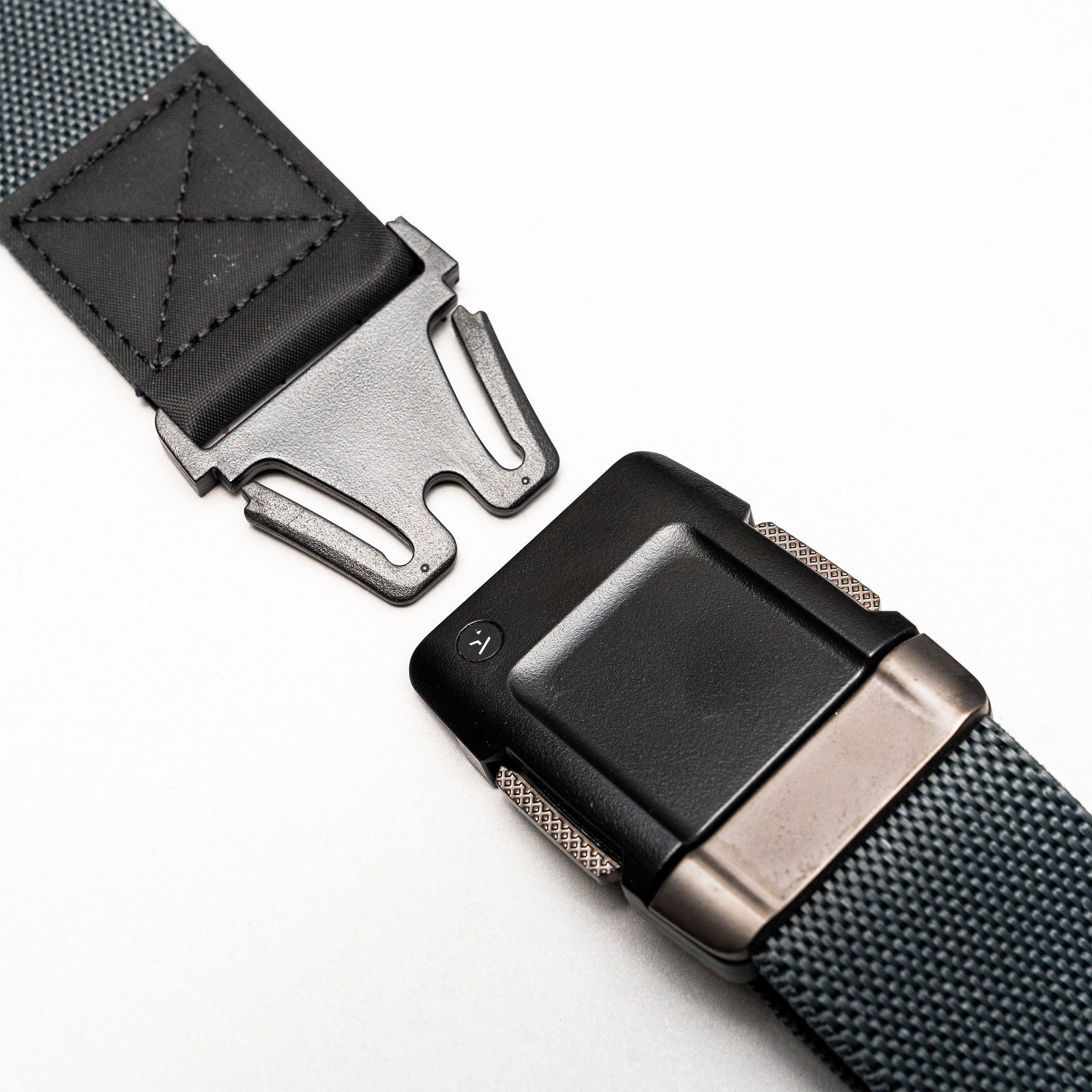 A close-up of the Arcade Belts Motion travel belt in black and gray, featuring a rectangular, low-profile buckle with a secure locking mechanism. The partially unclasped belt is displayed on a white background, ideal for travelers.