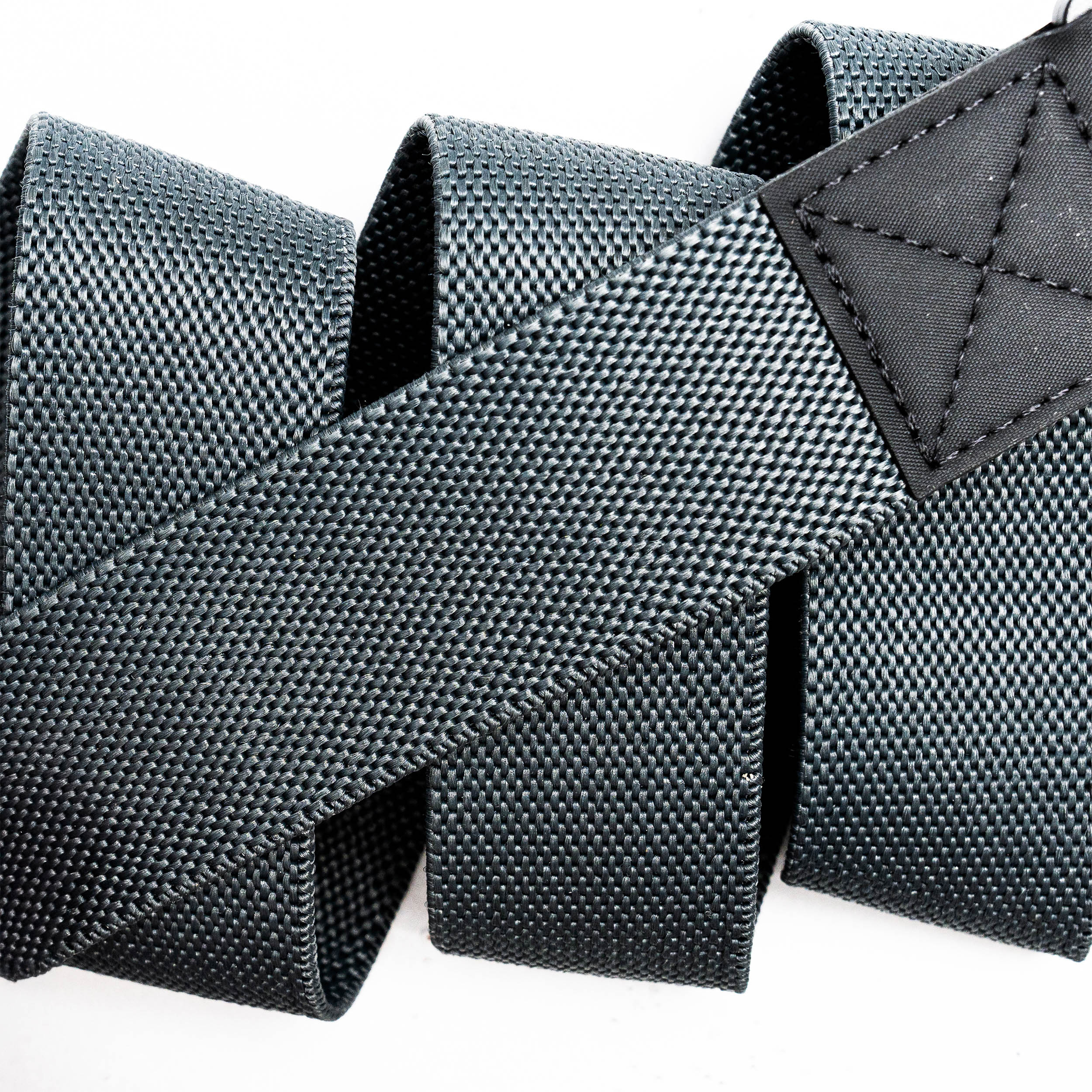 Close-up of a black, textured nylon strap from the Motion by Arcade Belts, looped in a zigzag pattern like a Low Profile Belt, featuring a stitched rectangular black leather patch at one end on a white background.
