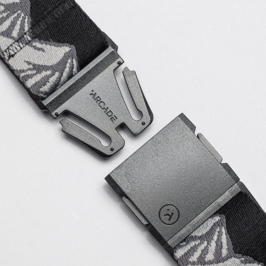 A close-up of the Arcade Belts POW x Joseph Toney, a black belt with gray and white patterns, features an open black buckle and ARCADE branding, showcasing its low-profile design.
