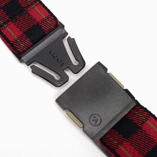 A close-up of the Arcade Belts Plaid features a black metal buckle with ARCADE branding on a red and black plaid stretch webbing strap. The low-profile buckle shows a small logo, and the parts are separated.