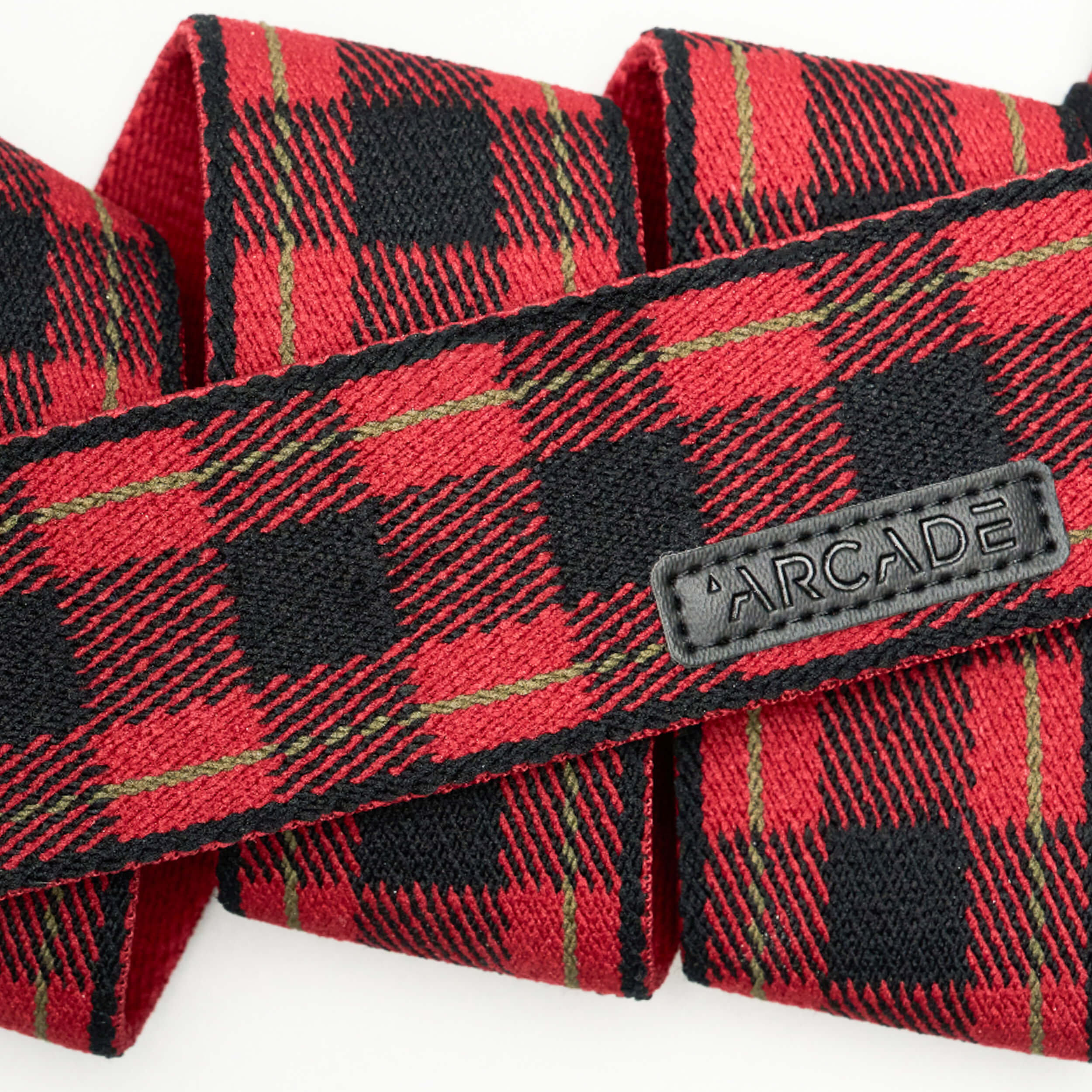 A close-up of Arcade Belts Plaid, a red and black stretch webbing belt, featuring a stitched black label reading ARCADE.